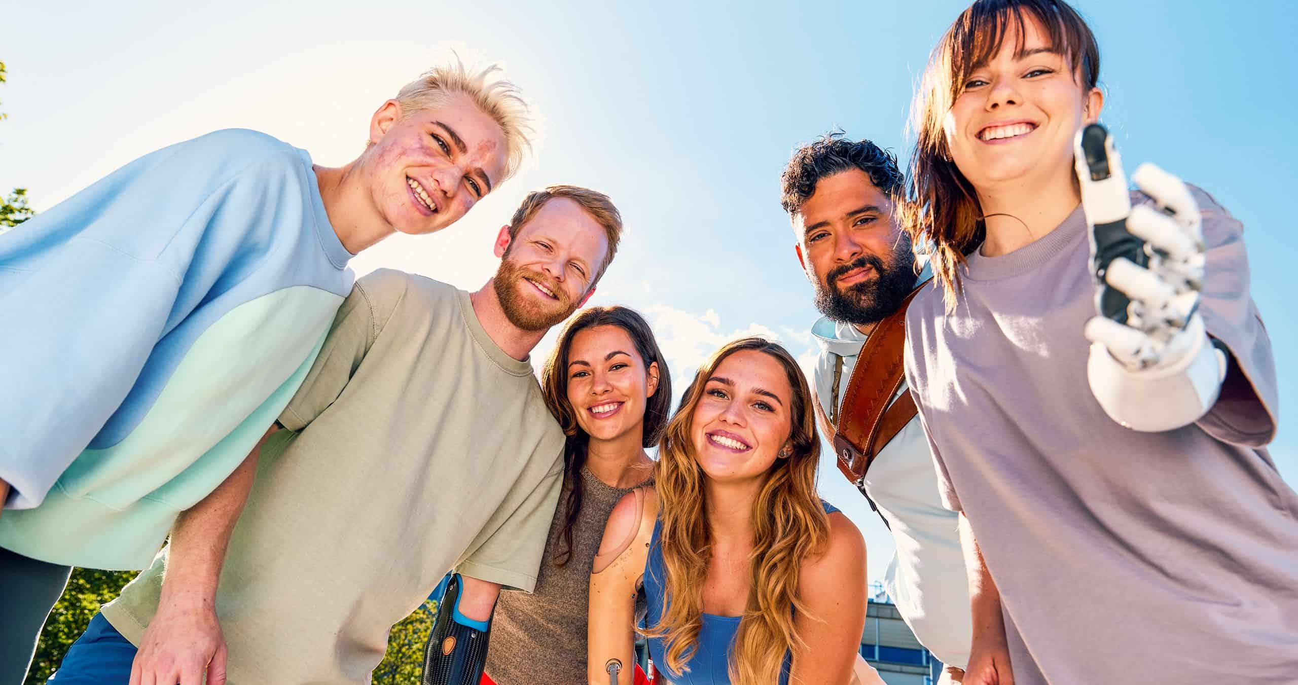 Groupe de jeunes adultes appareillés avec des prothèses, souriant ensemble en plein air sous un ciel bleu